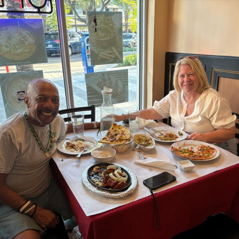 Two happy customers enjoying Indian cuisine at a table by a window at Sajna Indian Cuisine.