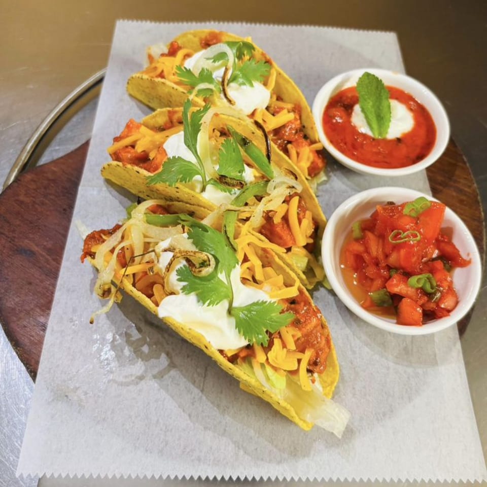 Three hard-shell tacos with meat, cheese, sour cream, and cilantro, served with two side sauces.