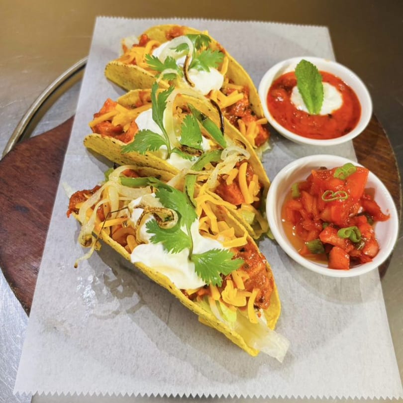 Three hard-shell tacos with meat, cheese, sour cream, and cilantro, served with two side sauces.