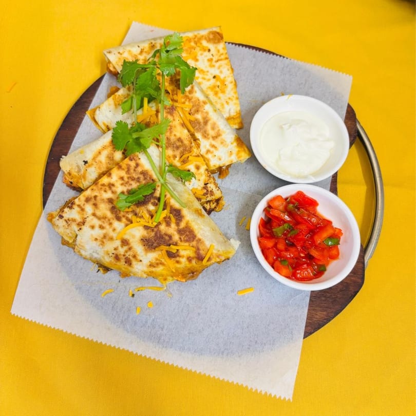 Sajna Indian Cuisine's quesadillas with cilantro, shredded cheese, salsa, and sour cream on a wooden platter.