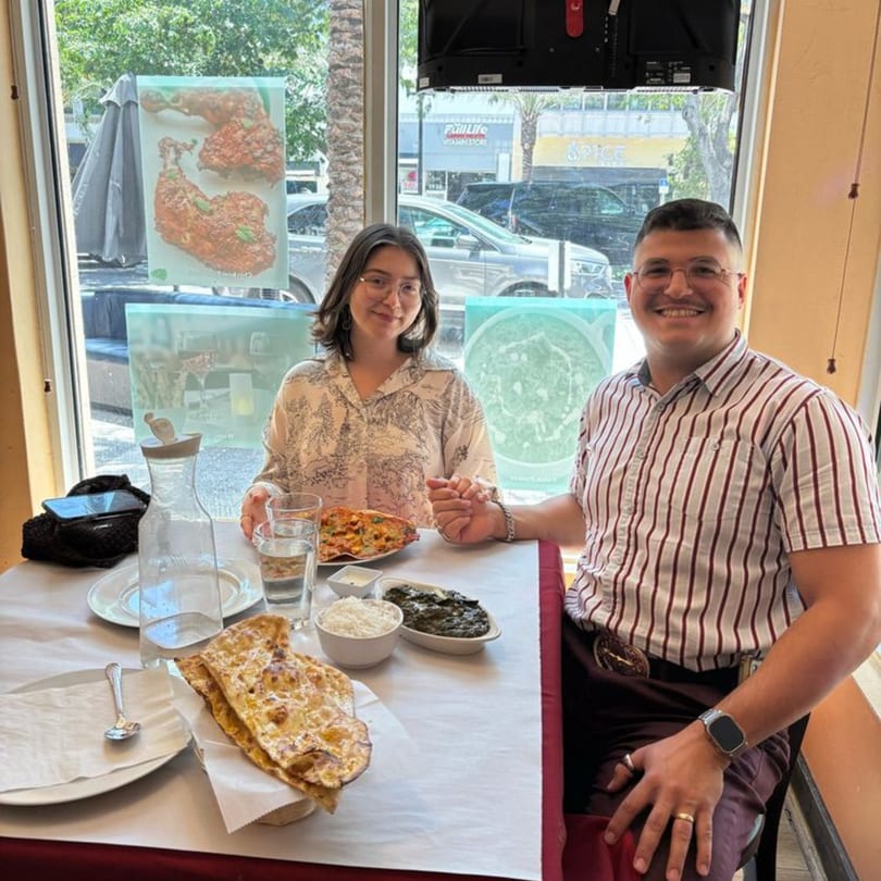 A smiling couple holding hands at a table with Indian food, including naan, rice, and a curry.