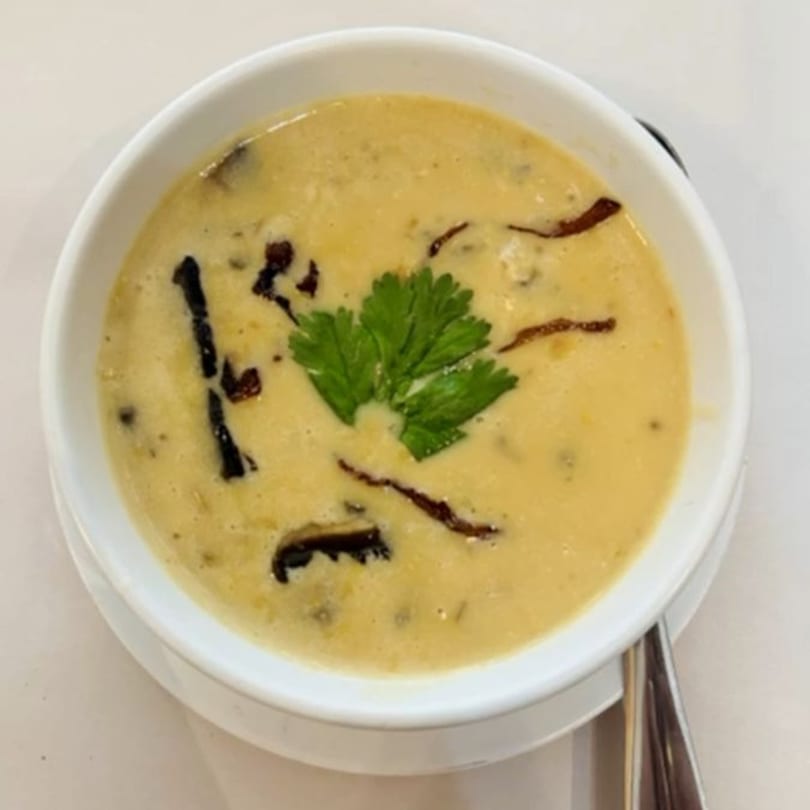 Creamy yellow Indian soup with dark mushroom pieces and a fresh green herb garnish in a white bowl.