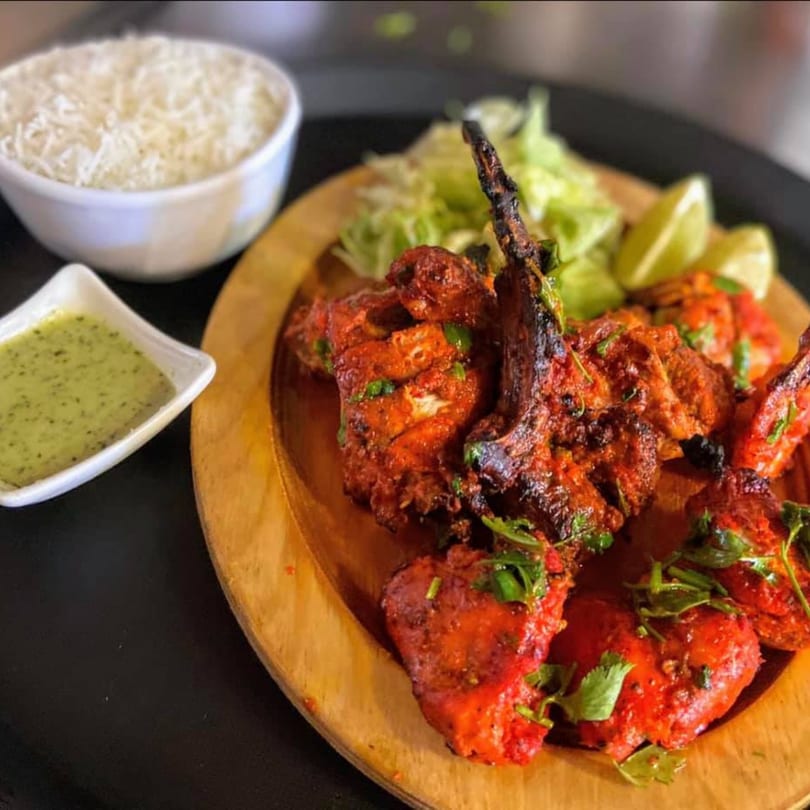 Sajna Indian Cuisine's Tandoori chicken and lamb chops with rice, green sauce, and lime wedges.