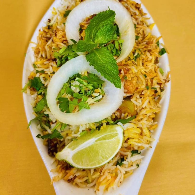 Sajna Indian Cuisine's chicken biryani, garnished with onion rings, mint, cilantro, and a lime wedge.