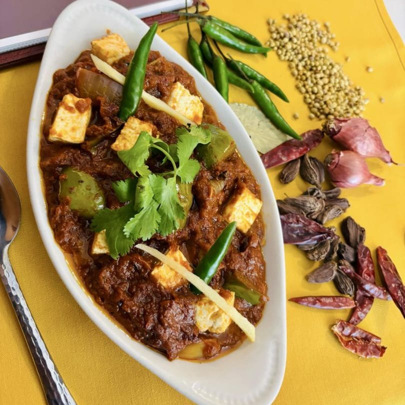 Sajna Indian Cuisine's paneer dish, garnished with cilantro, chilies, and ginger, surrounded by spices.
